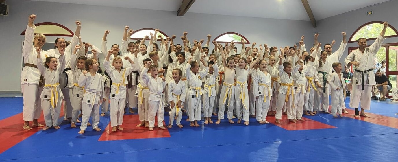 Le club au complet sur les tatamis bleus et rouges du dojo Jean Monnet : une soixantaine d'enfants et d'adultes en karategi lèvent le poing en souriant.