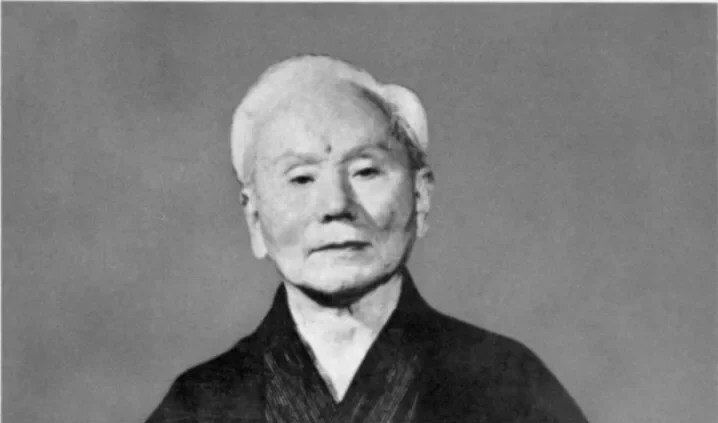 Portrait en noir et blanc de Gichin Funakoshi, fondateur du karaté Shotokan, en kimono sombre.